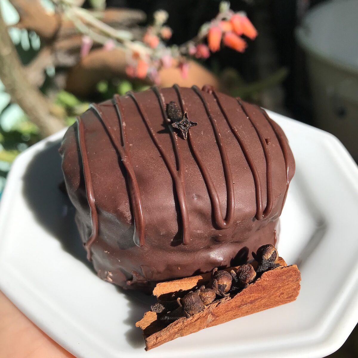 Pão de mel coberto de chocolate meio amargo, num prato branco com canela em pau e cravos